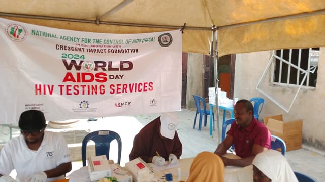 NACA/CIF World AIDS Day banner at outreach tent, team seated at registration table
